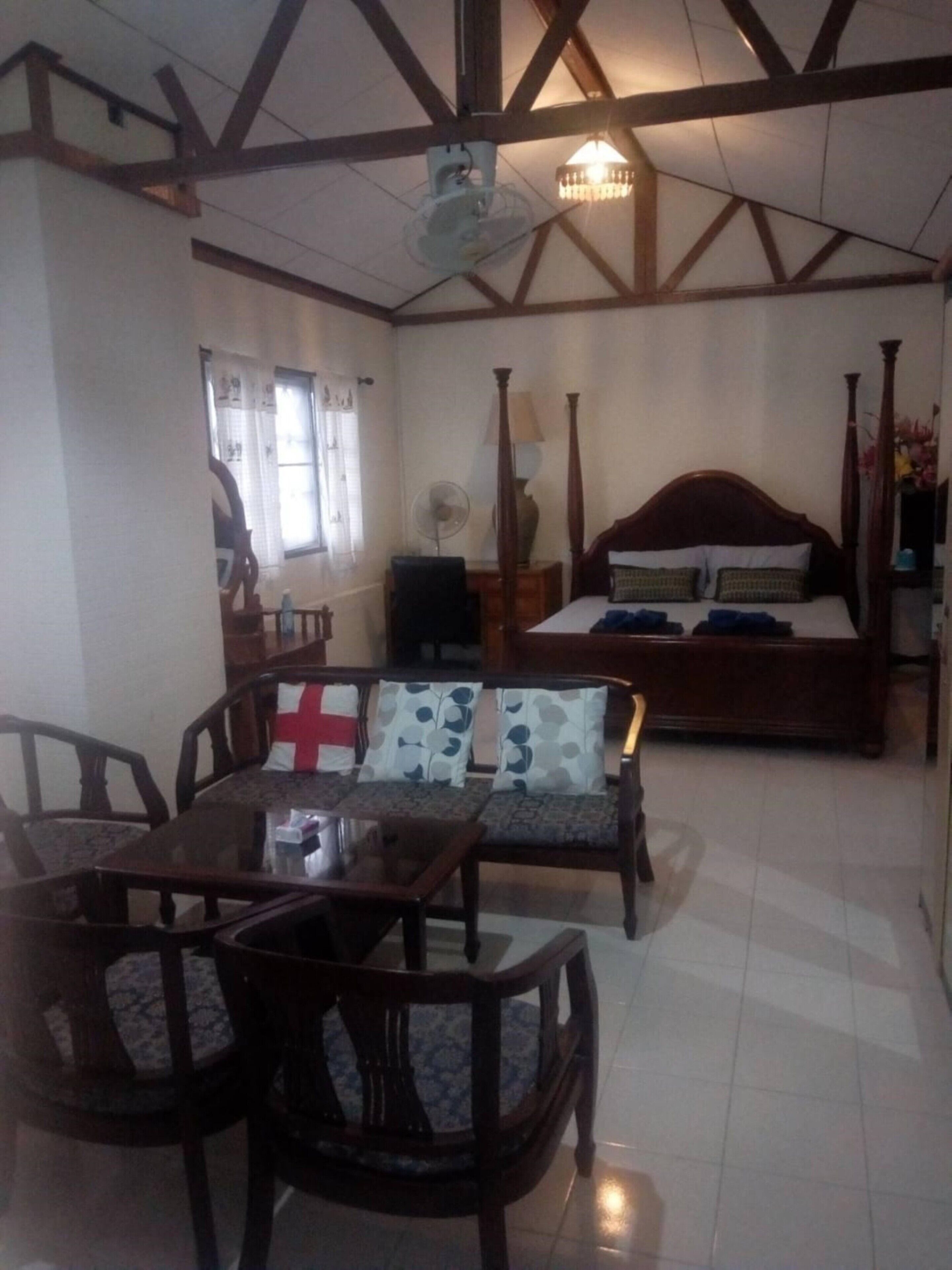 A room with a bed, a sofa, a dining table with chairs, a fan, and a chandelier.