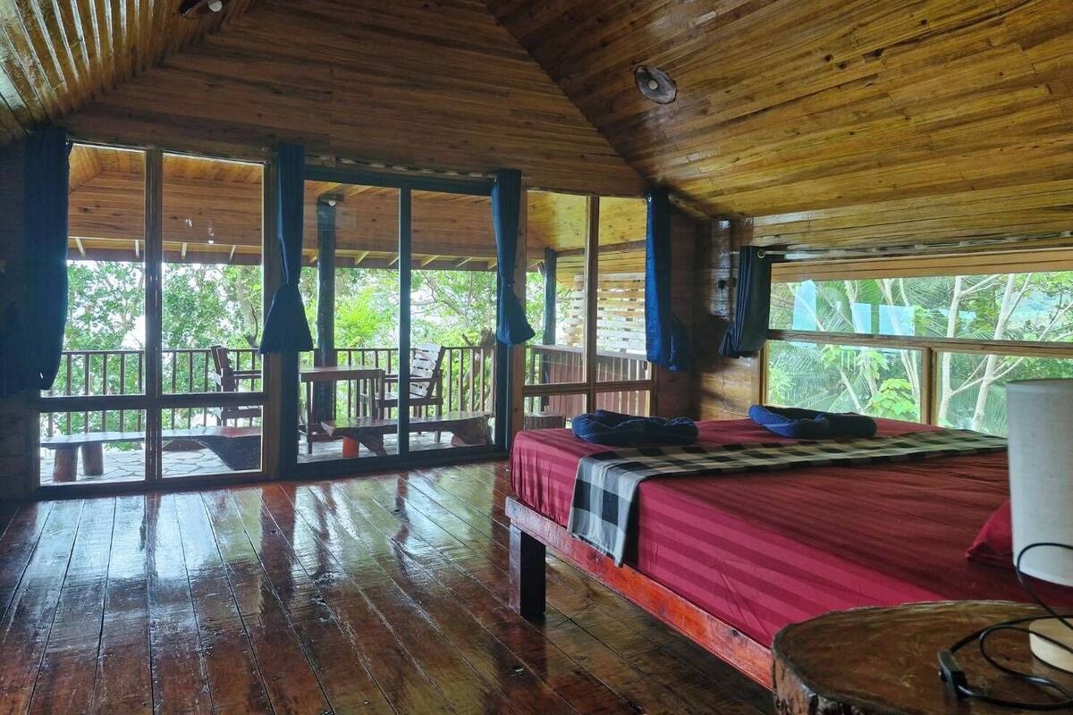 A wooden cabin with a bed, a table, and a balcony with chairs.