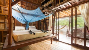 Una cama de madera con mosquitero, suelo de madera y vistas al exterior a través de amplias ventanas.