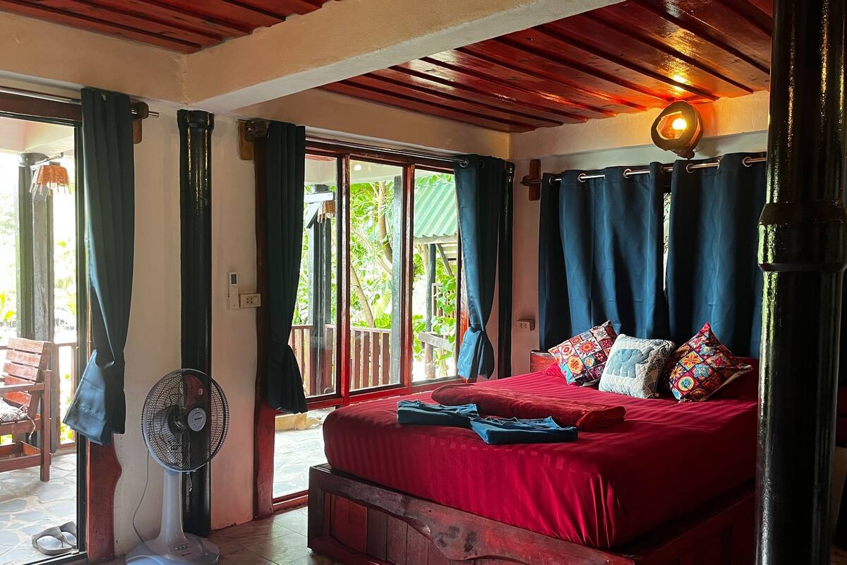 A bedroom with a wooden bed, red bedding, and a fan.
