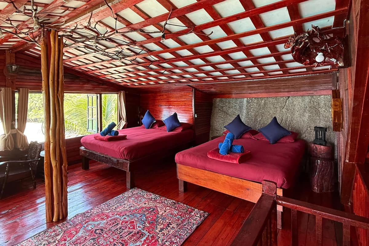 A room with two beds, a patterned rug, and a wooden ceiling structure.