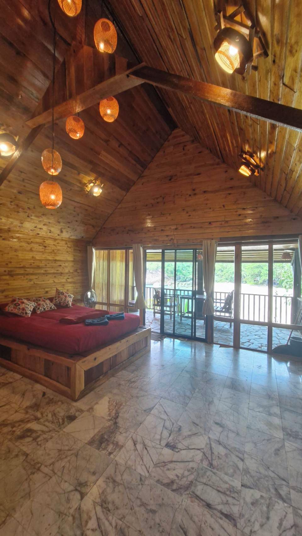 A spacious room with a wooden ceiling, a red sofa, and a large window offering a view of the outdoors.