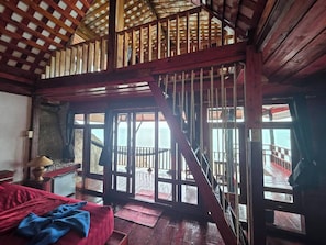 A room with a wooden staircase, a bed, a small table, and a view of the sea. - Mai Pen Rai Bungalows (Ko Pha-ngan)