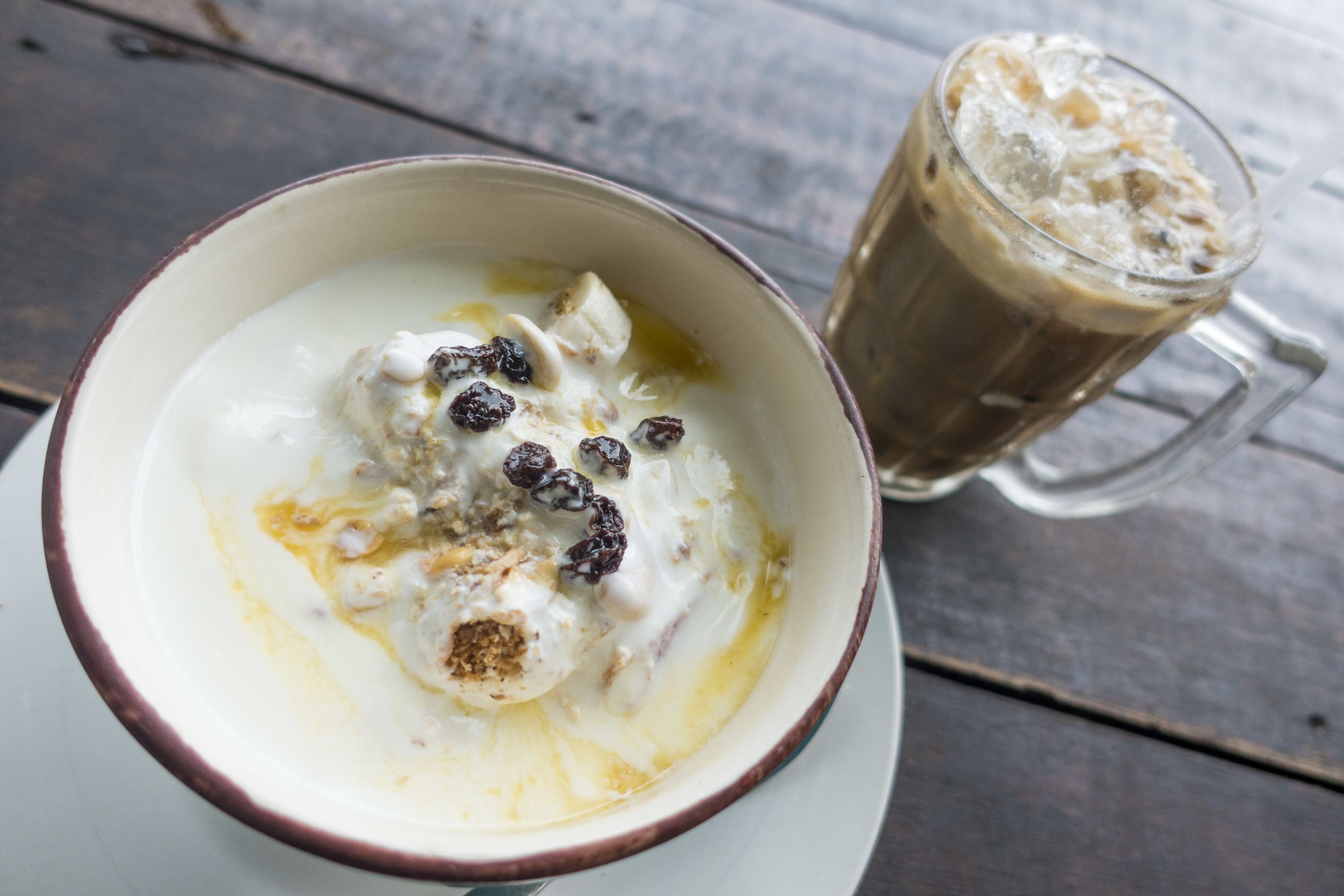 A bowl of yogurt with berries and a glass of iced coffee on a wooden table.