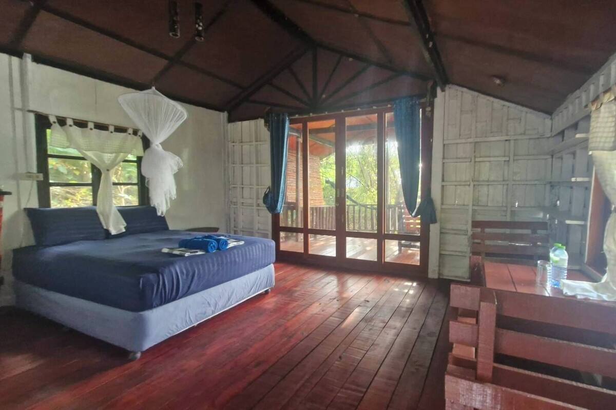 A room with a bed, a wooden bench, and a view through a window.