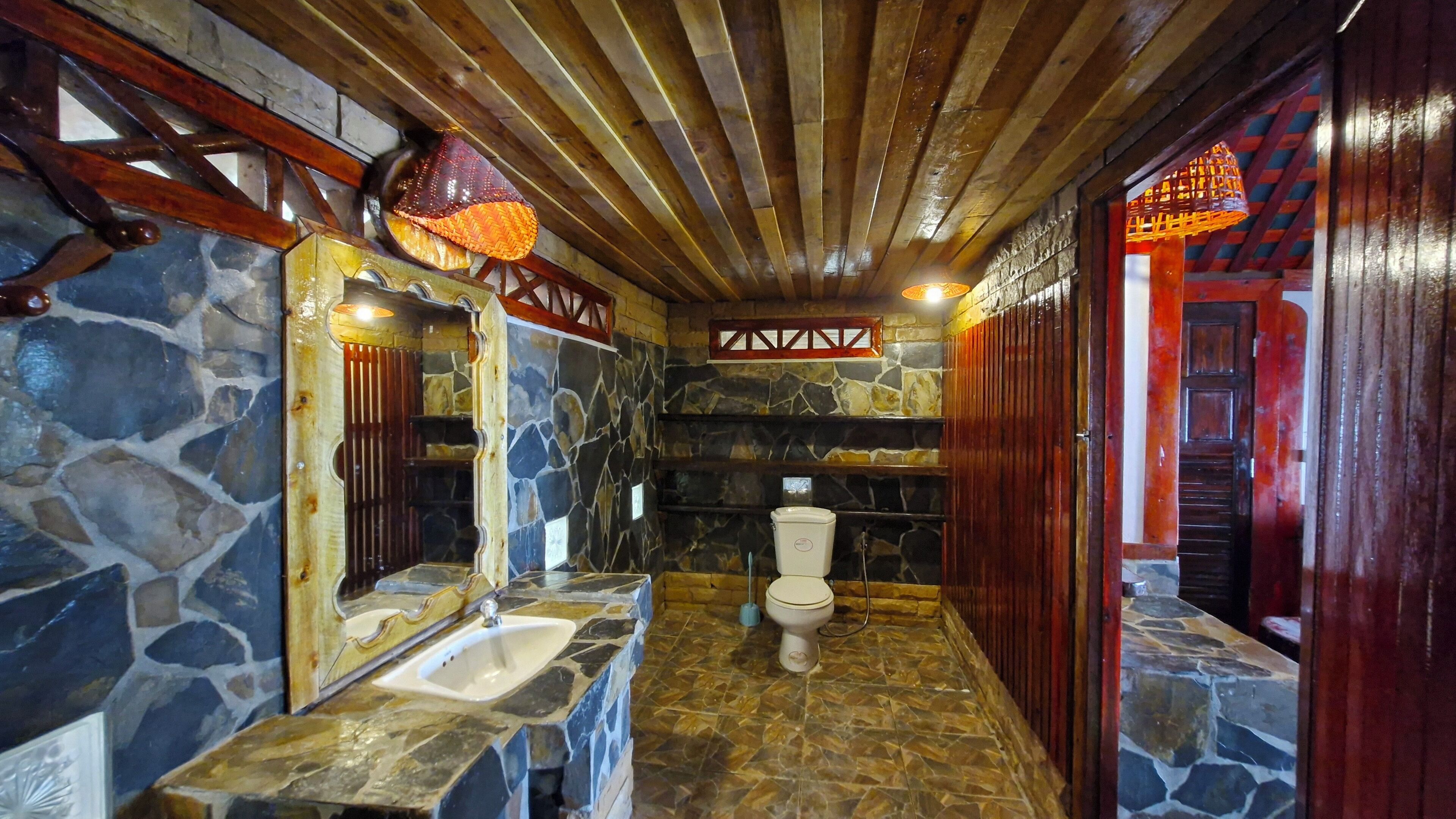A bathroom with stone walls, a wooden ceiling, and a toilet.