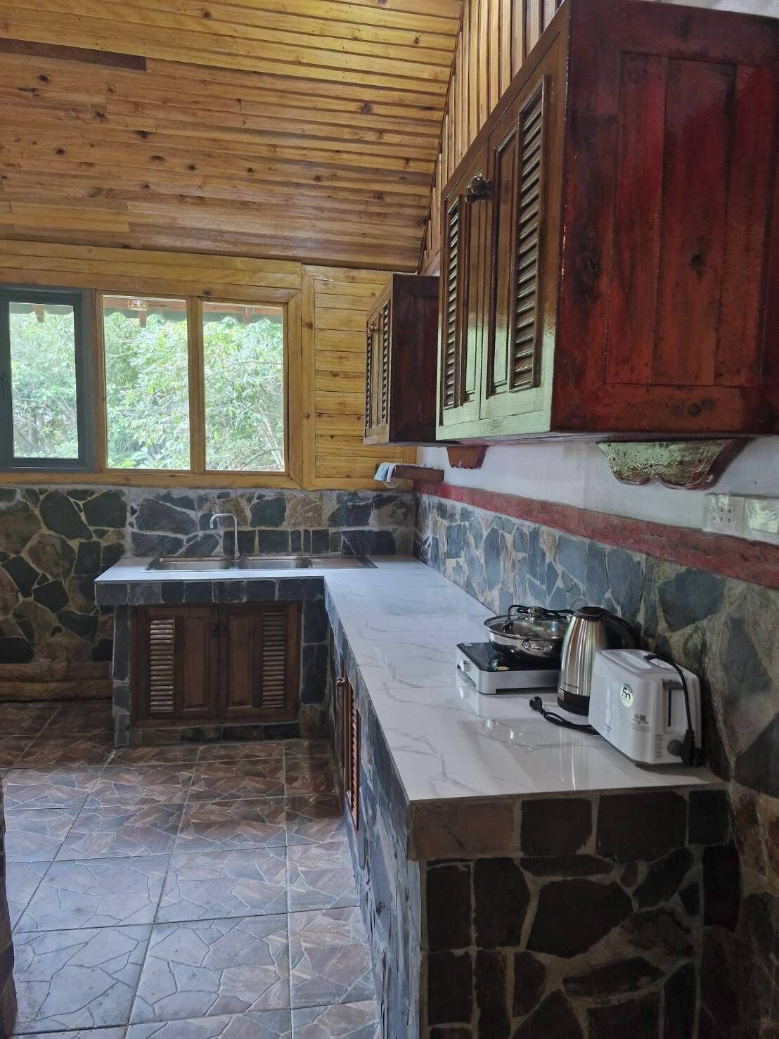 Una cocina con encimera de piedra, armarios de madera y ventana con vistas a la vegetación.