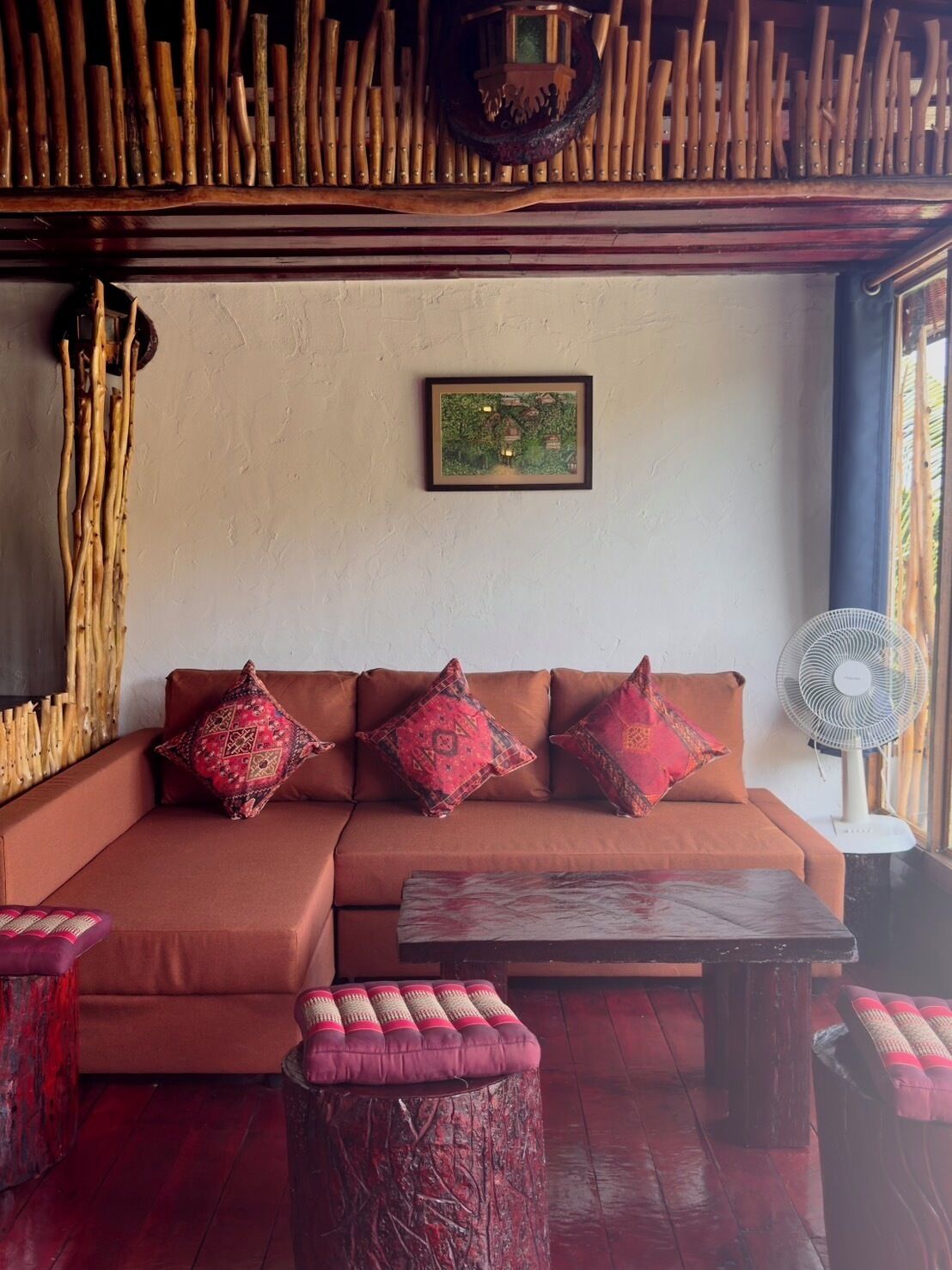 A cozy room with a brown sofa, patterned cushions, a small table, and a fan.