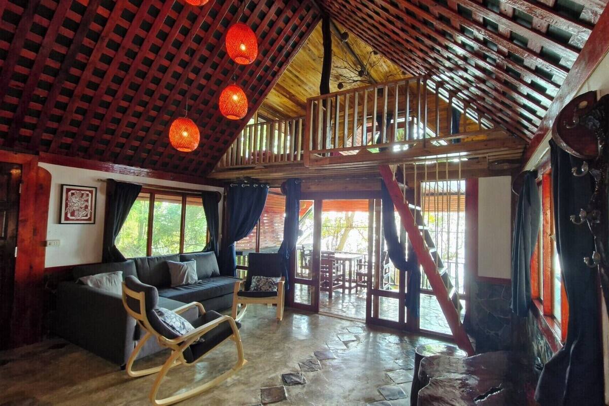 A rustic cabin interior with a loft bedroom, wooden floors, and a cozy seating area.