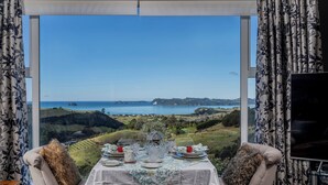 A dining table set with plates, glasses, and a centerpiece, overlooking a scenic landscape with hills and a body of water.