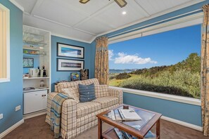 A living room with a sofa, a coffee table, and a view of a landscape through a window. - Bayview Valley Lodge (Whitianga)