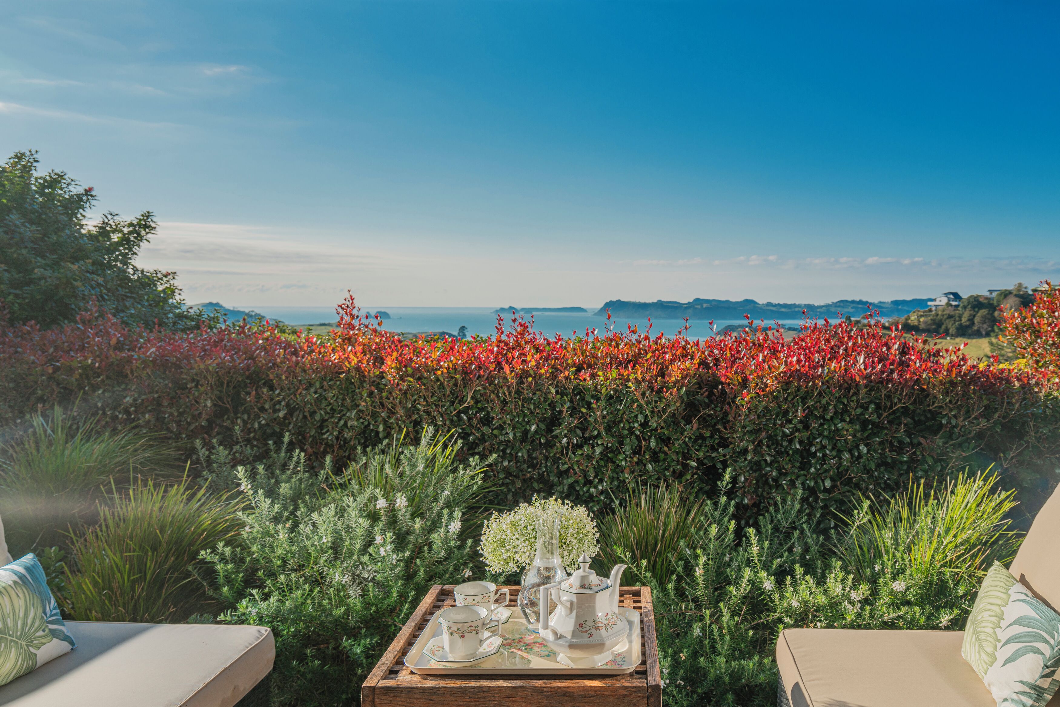 A garden patio with a tray of tea set and a view of the sea.