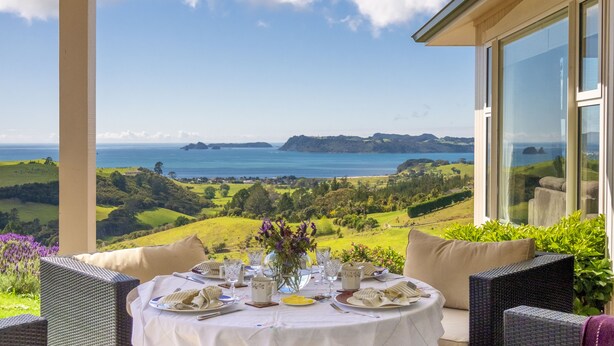 A dining table set for two with a view of the sea and hills.