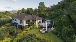 A modern house with a spacious patio, surrounded by lush greenery and hills.