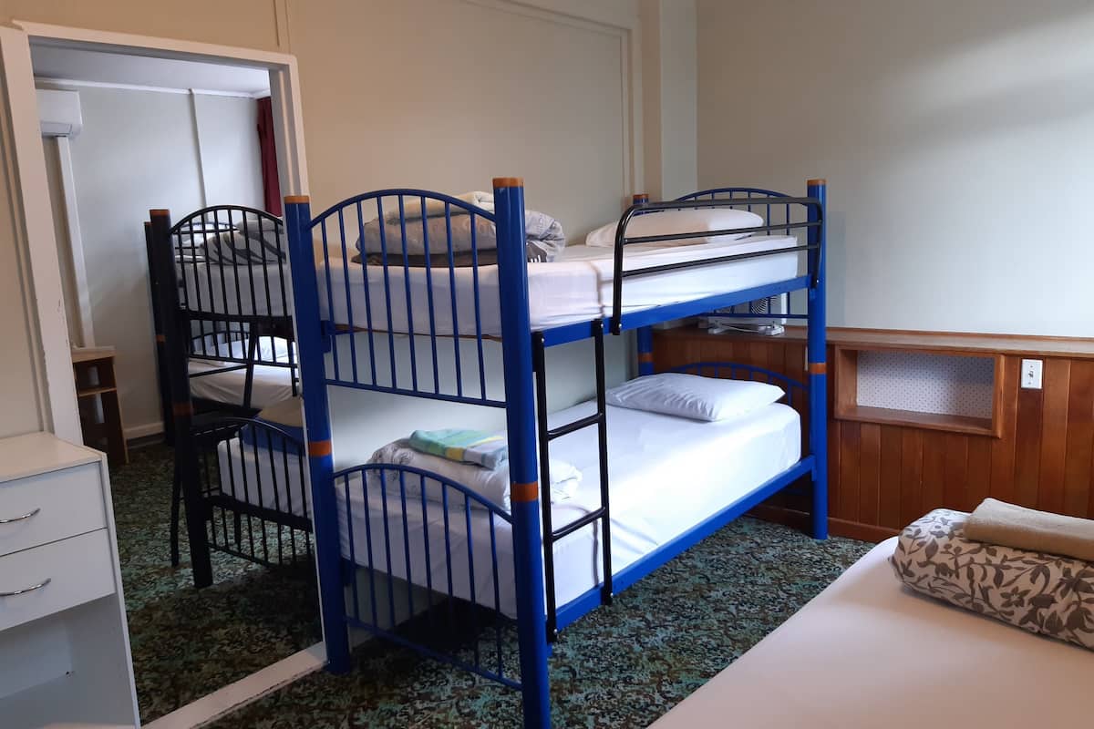 A bunk bed room with a desk, a wardrobe, and a patterned carpet.