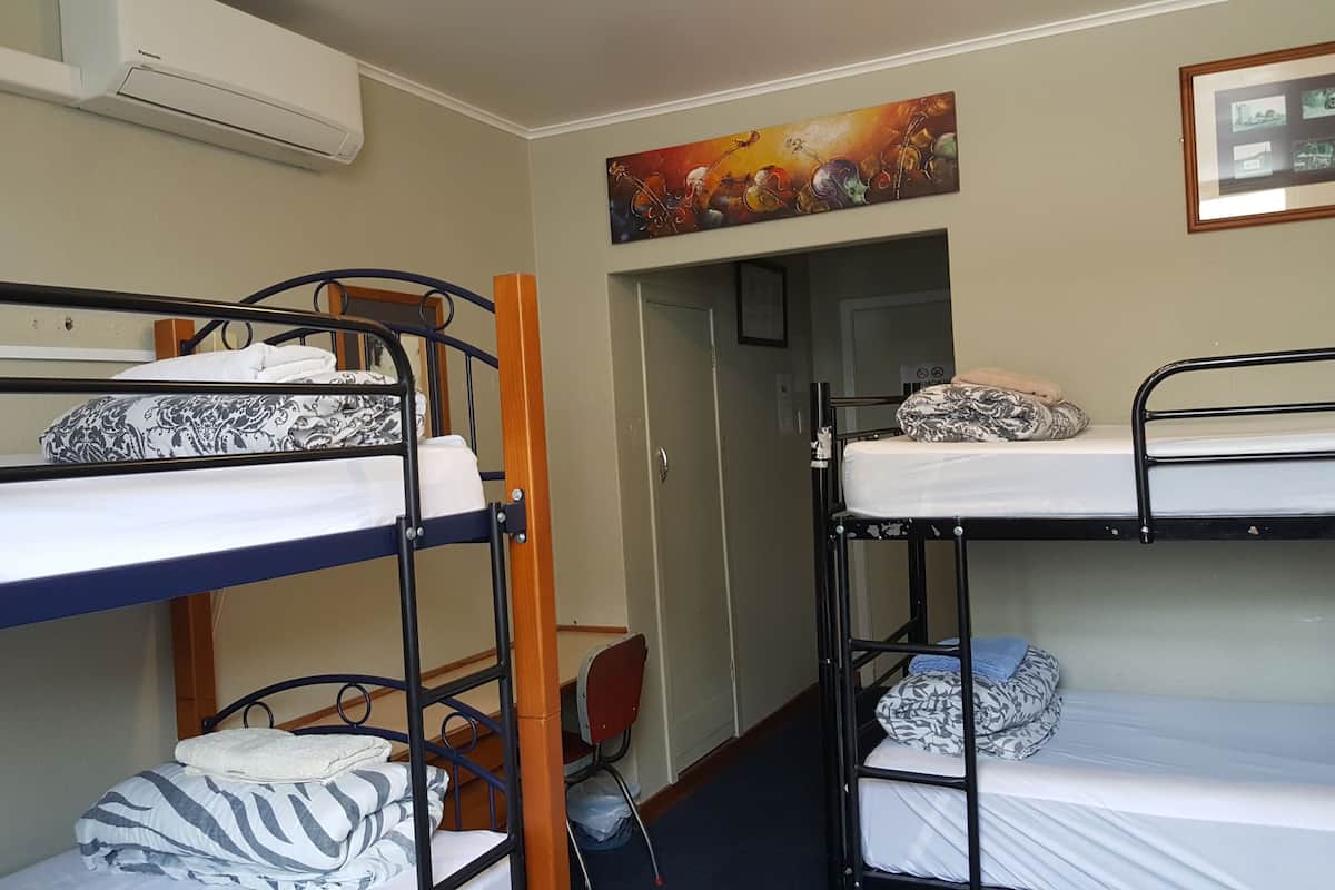 A dormitory room with bunk beds, a painting on the wall, and a door leading to another room.
