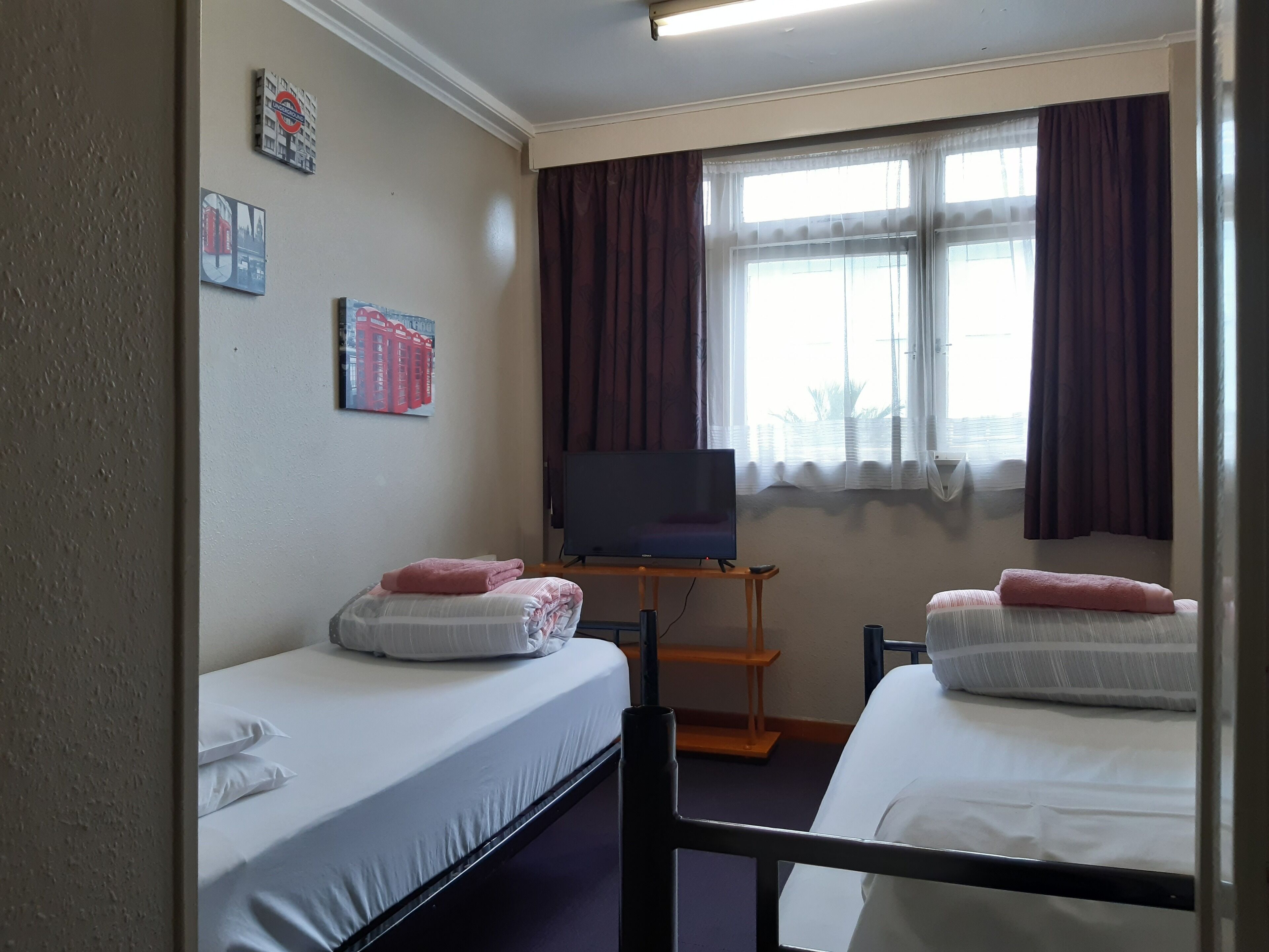 Habitación de hotel con dos camas individuales, un televisor sobre un soporte de madera y una ventana con cortinas.