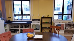 Cozinha com mesa de jantar, cadeiras e uma tigela de limões. Há janelas, uma pia e diversos eletrodomésticos.