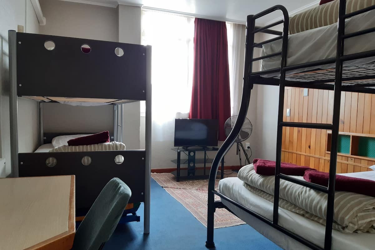 A bunk bed room with a desk and chair, a television, and a window with curtains.