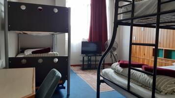 A bunk bed room with a desk and chair, a television, and a window with curtains.