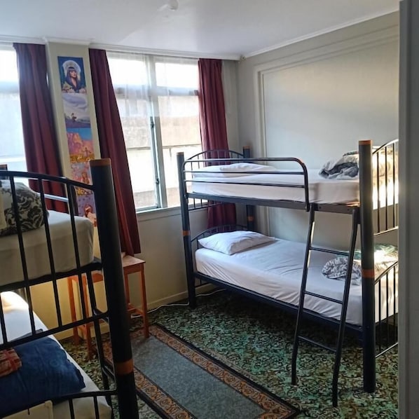 Habitación tipo dormitorio con literas, una silla, un ventanal con cortinas y un cartel en la pared.