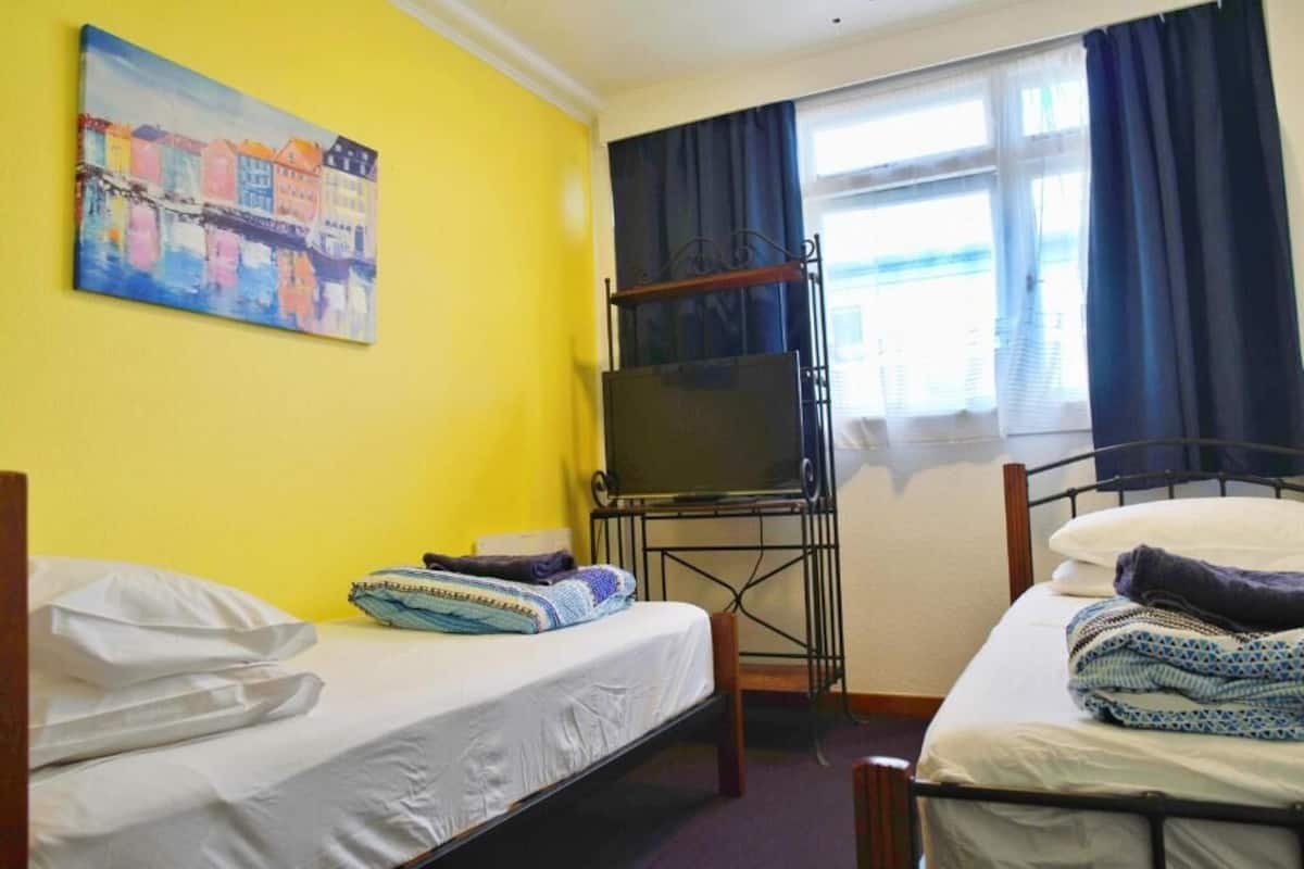 A room with two beds, a TV on a stand, and a painting on the wall.