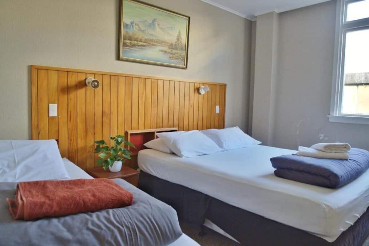 A hotel room with two beds, a wooden headboard, a painting, and a window.