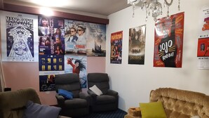 Sala de estar com um sofá marrom, uma poltrona reclinável e uma poltrona marrom. Há pôsteres de filmes na parede.