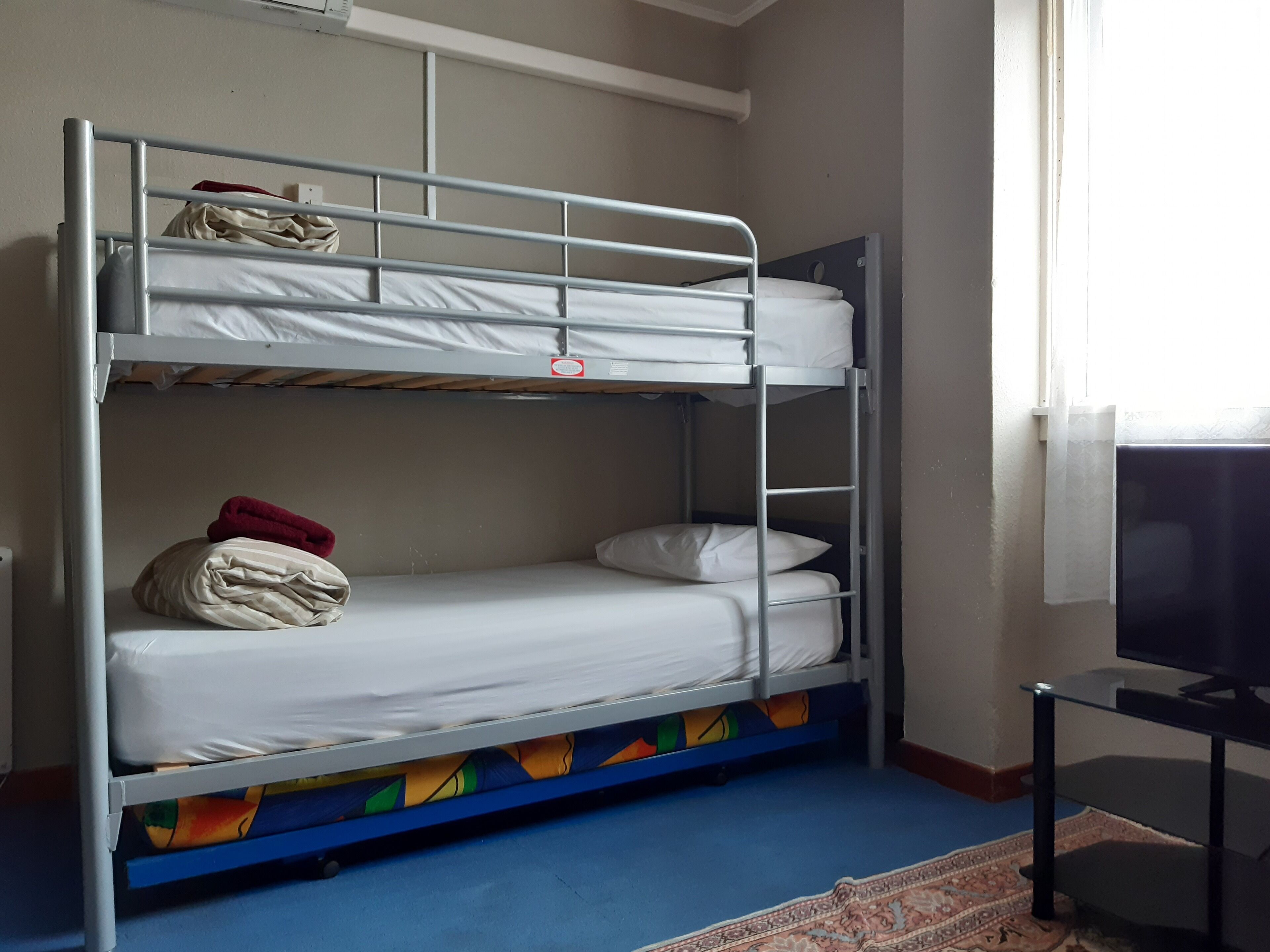 Una cama litera con un televisor sobre un soporte a la derecha.