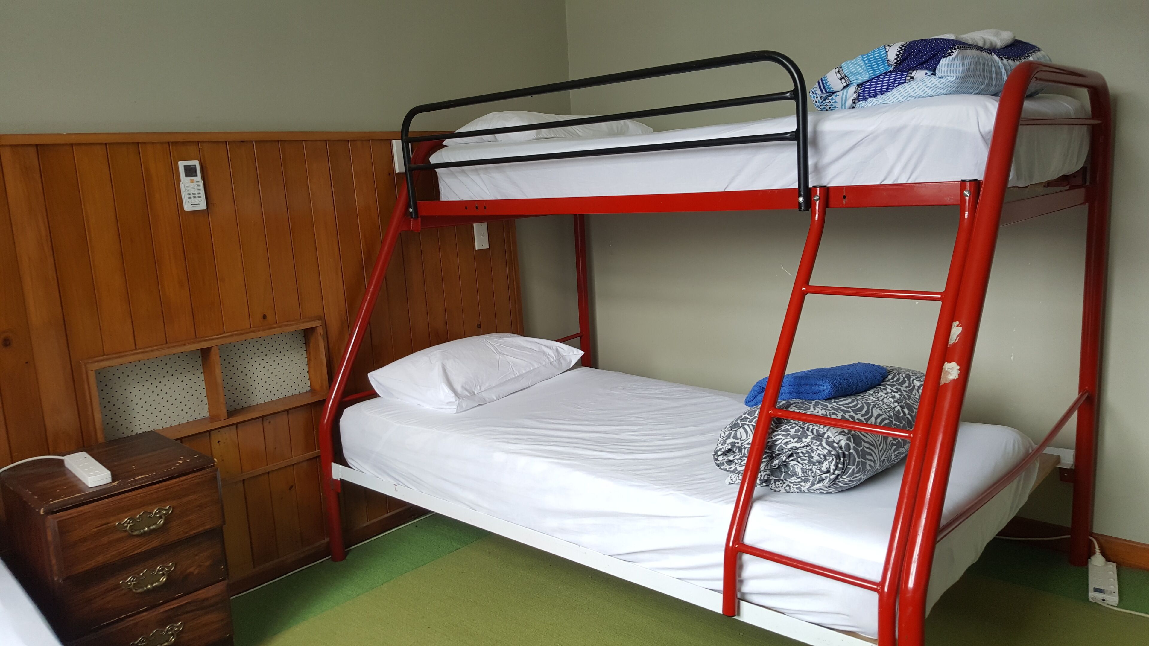 A bunk bed with a wooden headboard, a bedside table with drawers, and a green carpet.