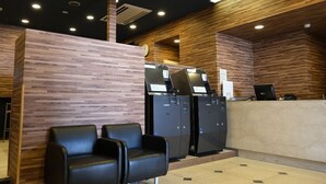 A reception area with a wooden wall, a reception desk, and two black chairs. - Swanky Hotel Otomo (Sapporo)