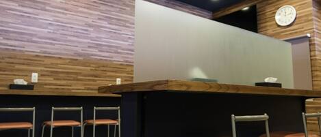 Una zona de bar con taburetes, mostrador de madera y un reloj en la pared.