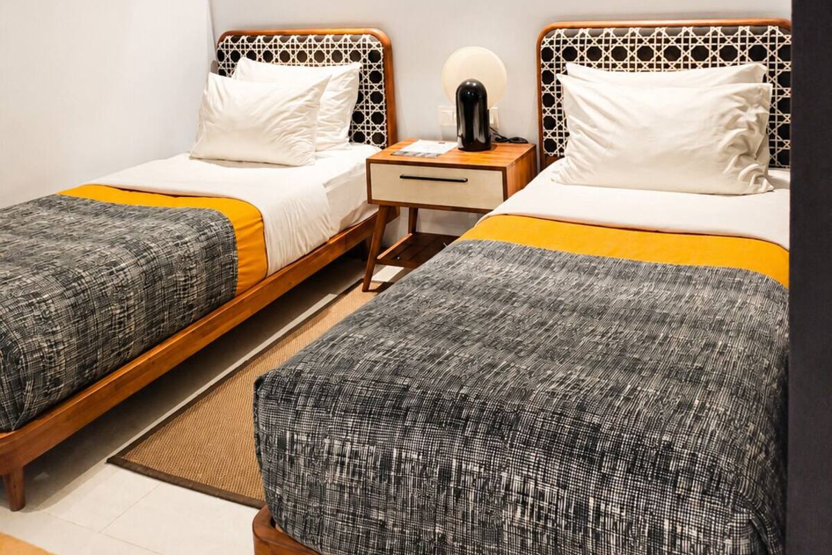 A hotel room with two beds, a bedside table with a lamp, and a large mirror reflecting the room.