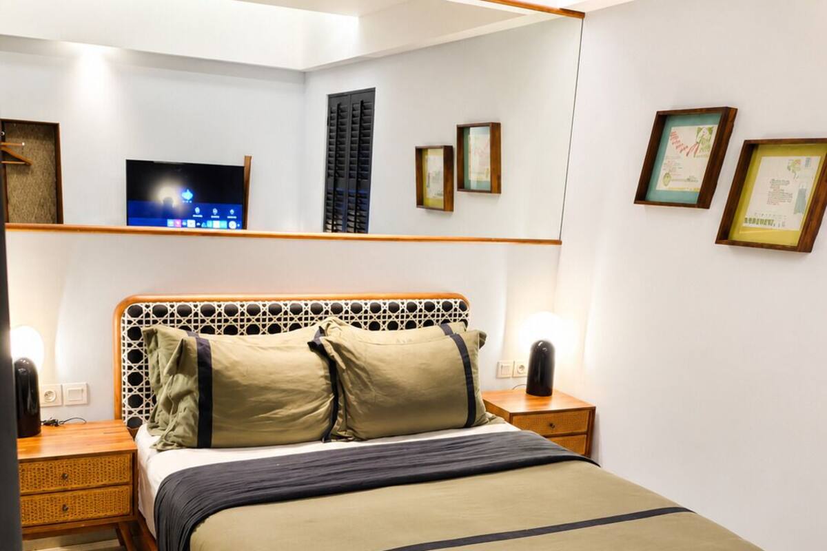 A bedroom with a bed, bedside tables, a TV, and framed pictures on the wall.
