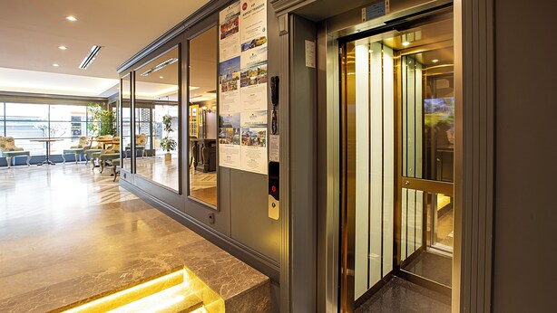 An elevator with a digital display, a reception area with seating, and a poster on the wall. - Aston Hotel Taksim (Istanbul)
