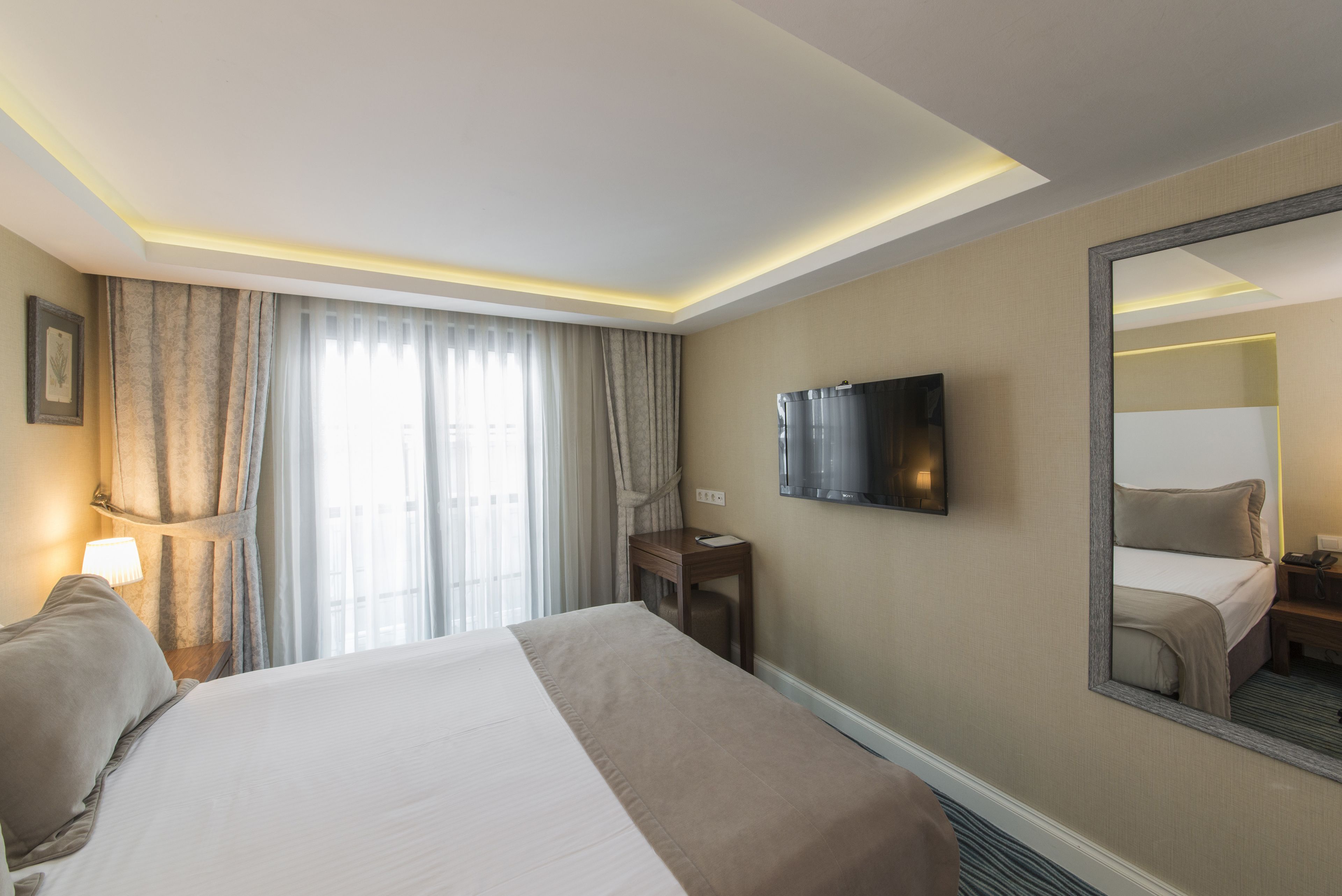 A hotel room with a large bed, a desk, a television, and a mirror.