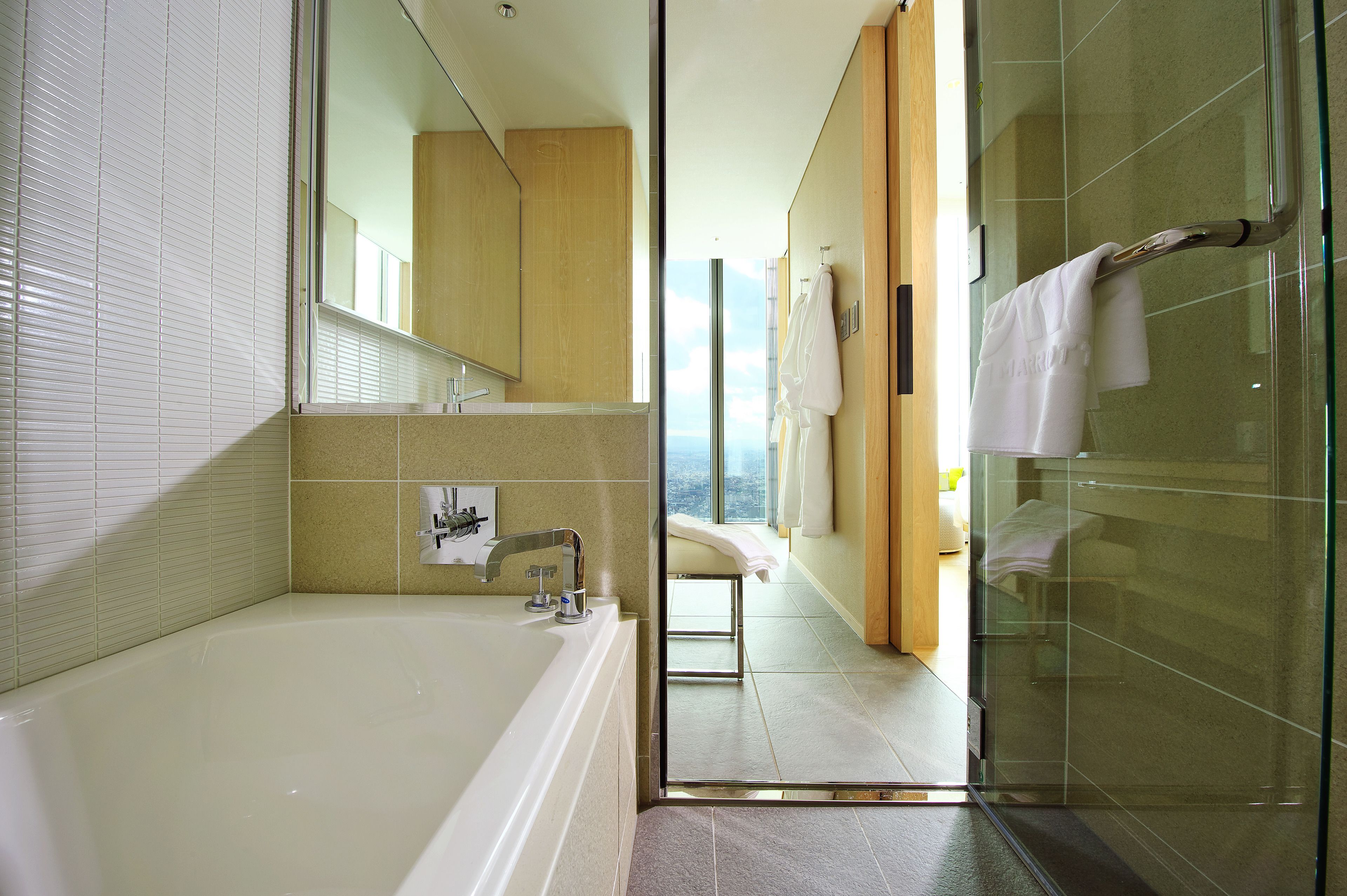 A modern bathroom with a bathtub, a glass shower enclosure, and a view of the city through a large window.
