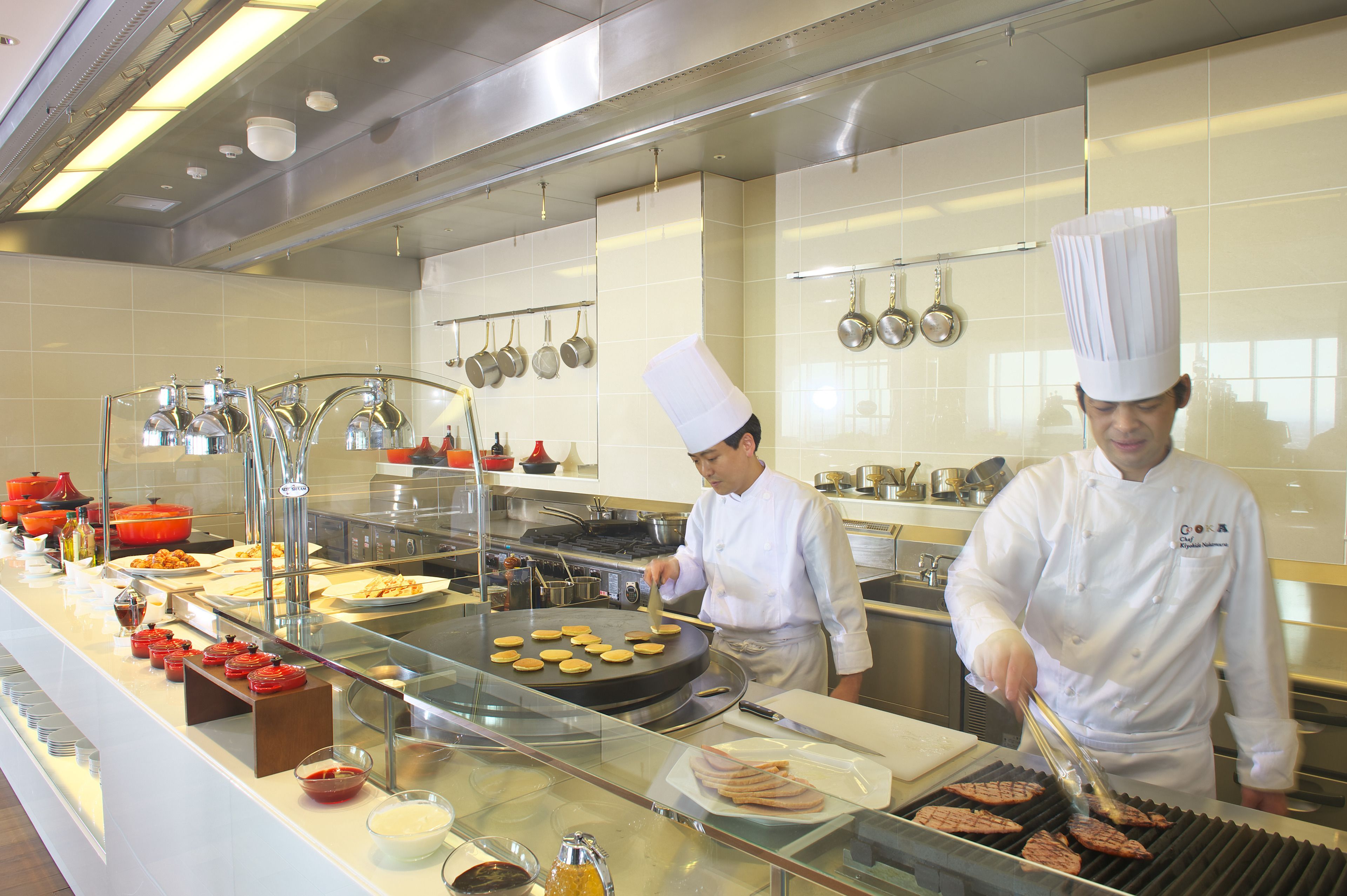 A kitchen with chefs preparing food, stainless steel appliances, and a buffet line with various dishes.