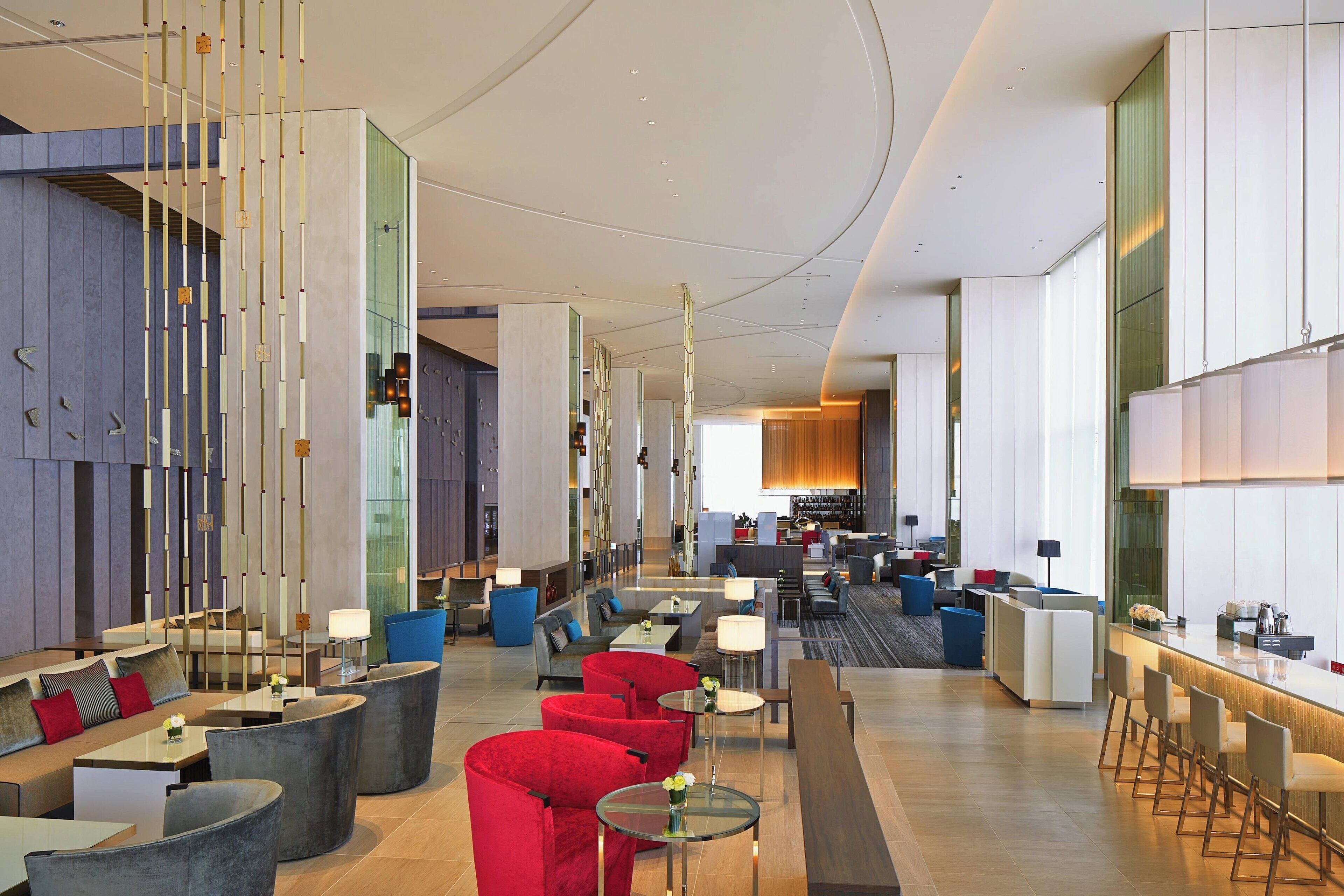 Eine moderne Hotelhalle mit Sitzbereichen, einer Bar und einer im Hintergrund sichtbaren Küche.