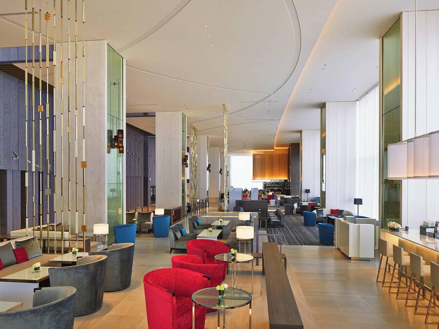 Un moderno vestíbulo de hotel con zonas de estar, un bar y una cocina visible al fondo.
