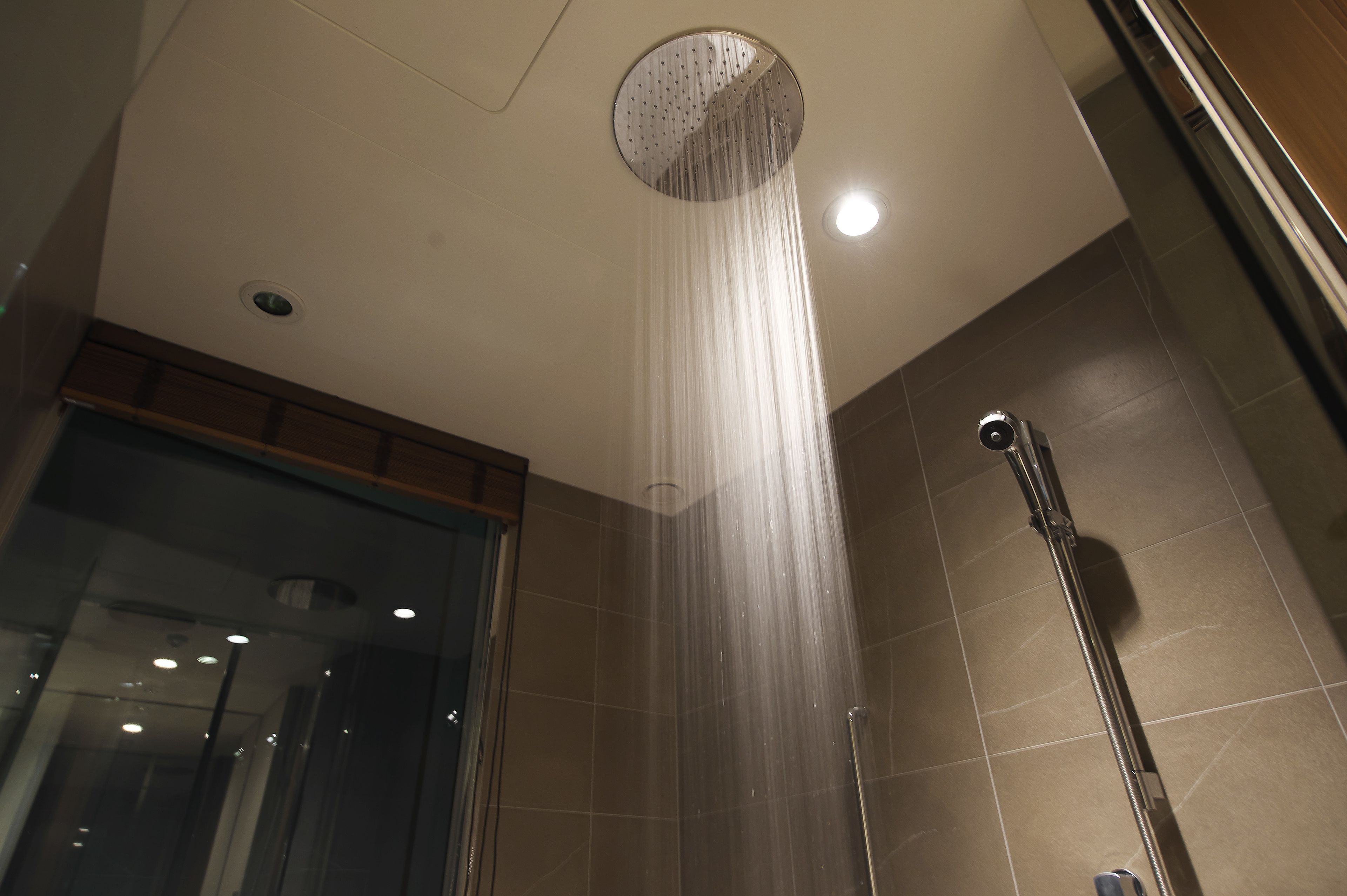 A modern shower with a circular rain showerhead, a handheld showerhead, and a glass door.