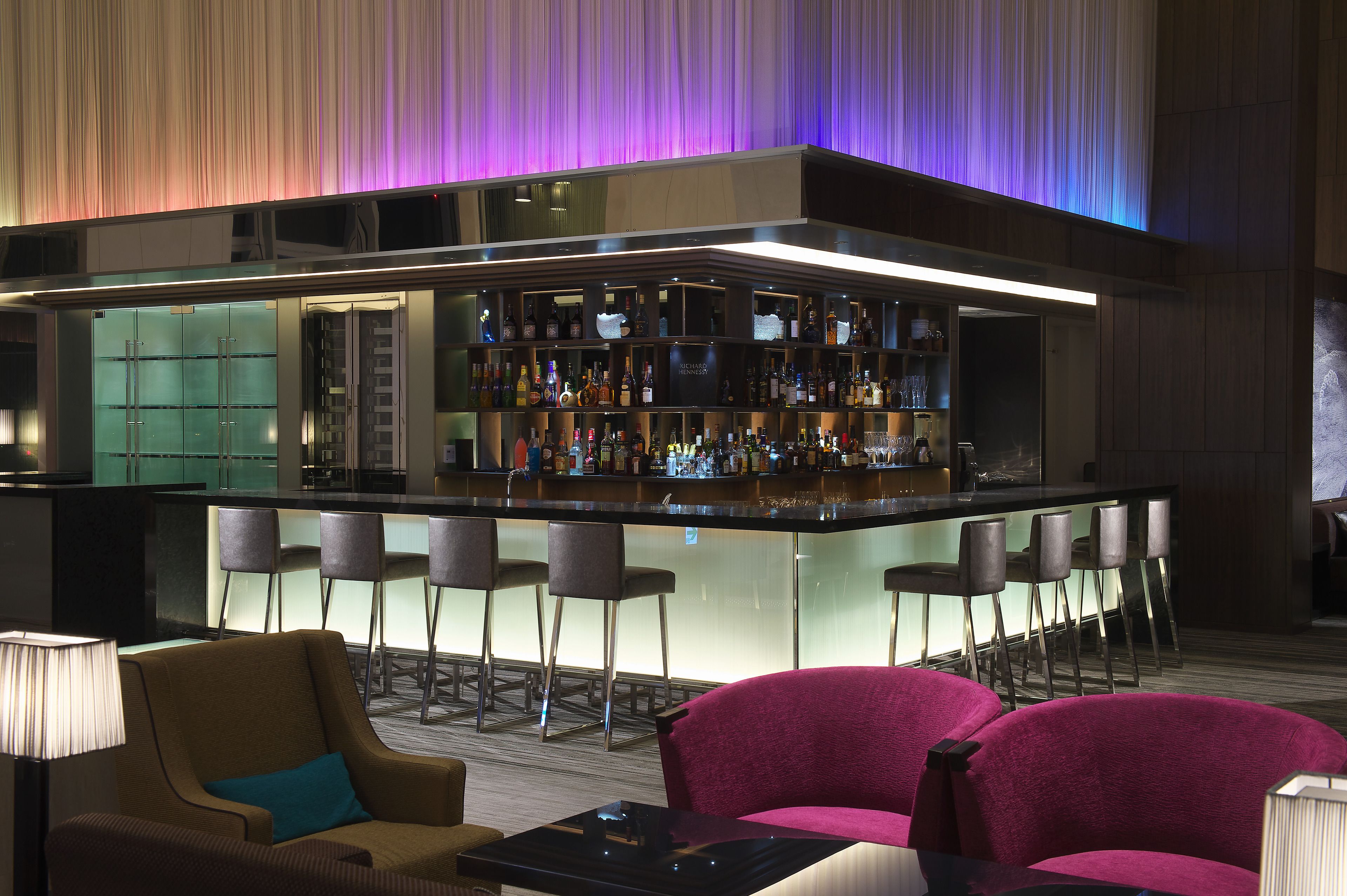 A bar area with a counter, stools, and a variety of bottles.
