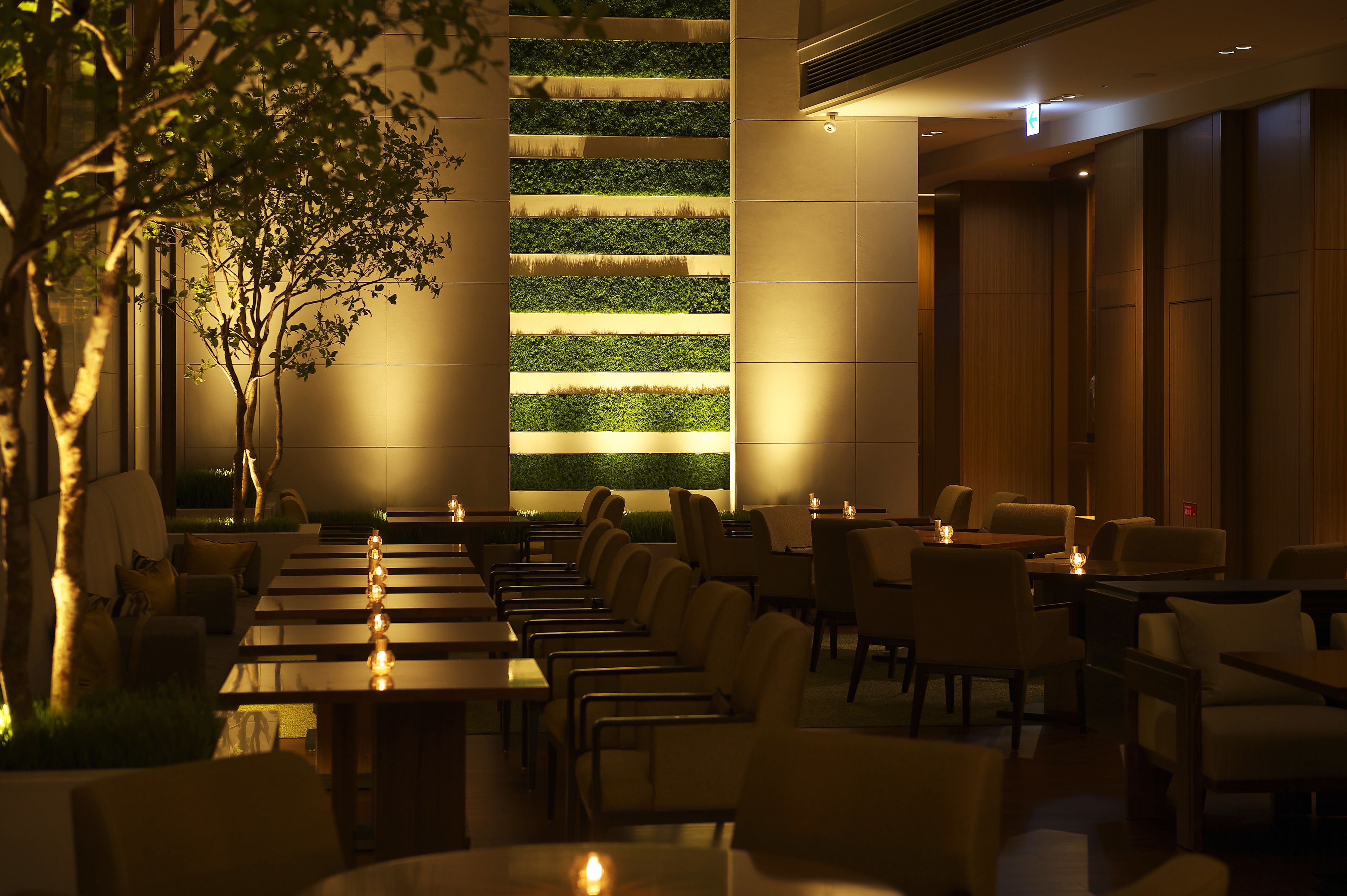A restaurant with long tables and chairs, a vertical garden wall, and a tree.