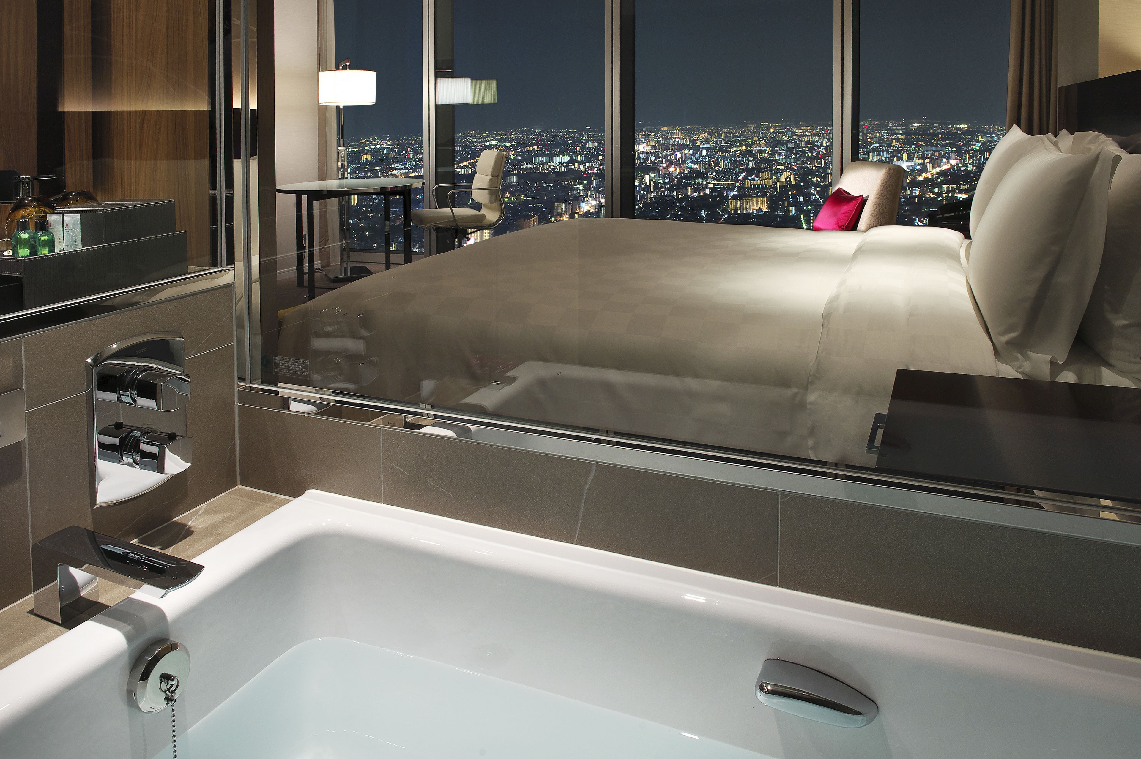 A modern hotel room with a large bed, a sitting area with a table and chairs, and a bathtub.