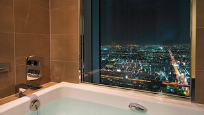 A modern bathroom with a bathtub, a glass-enclosed shower, and a view of a cityscape at night. - Osaka Marriott Miyako Hotel (Osaka)