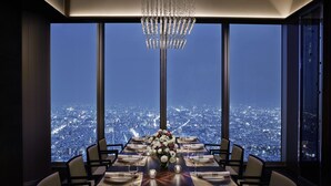 Et spisebord dækket til fire personer med en lysekrone hængende over, store vinduer med udsigt over byen.