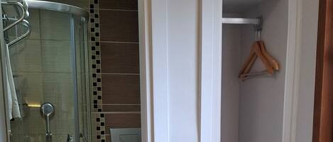 A bedroom with a bed, a shower, a toilet, and a small shelf with a hanging item.