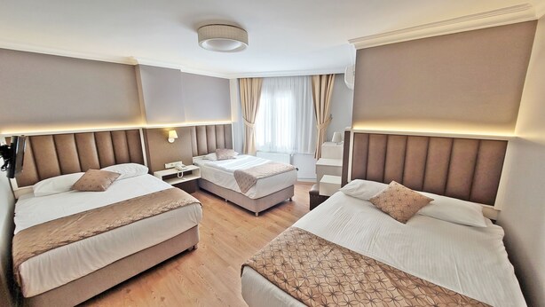 A hotel room with two beds, a nightstand, a lamp, and a window with curtains. - Hotel Sureyya (Istanbul)
