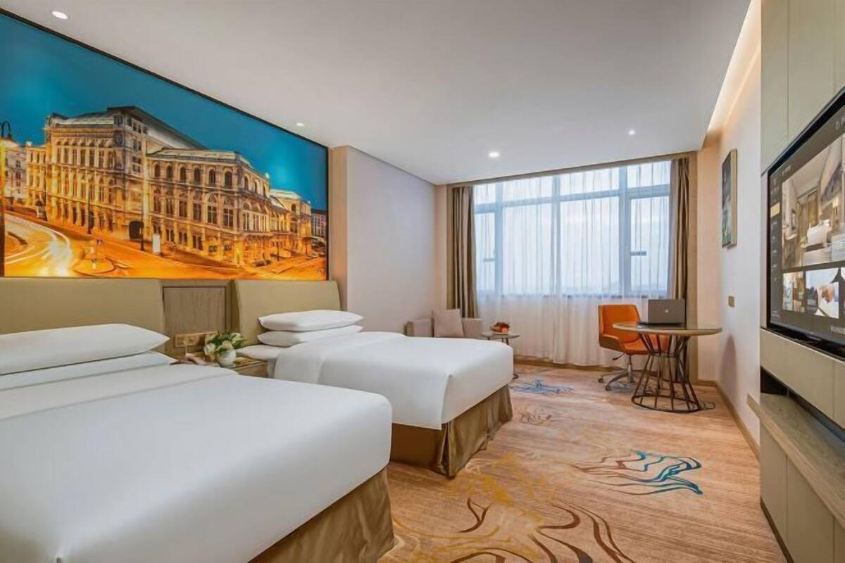 A hotel room with two beds, a large window, a desk with a chair, a television, and a mural on the wall.