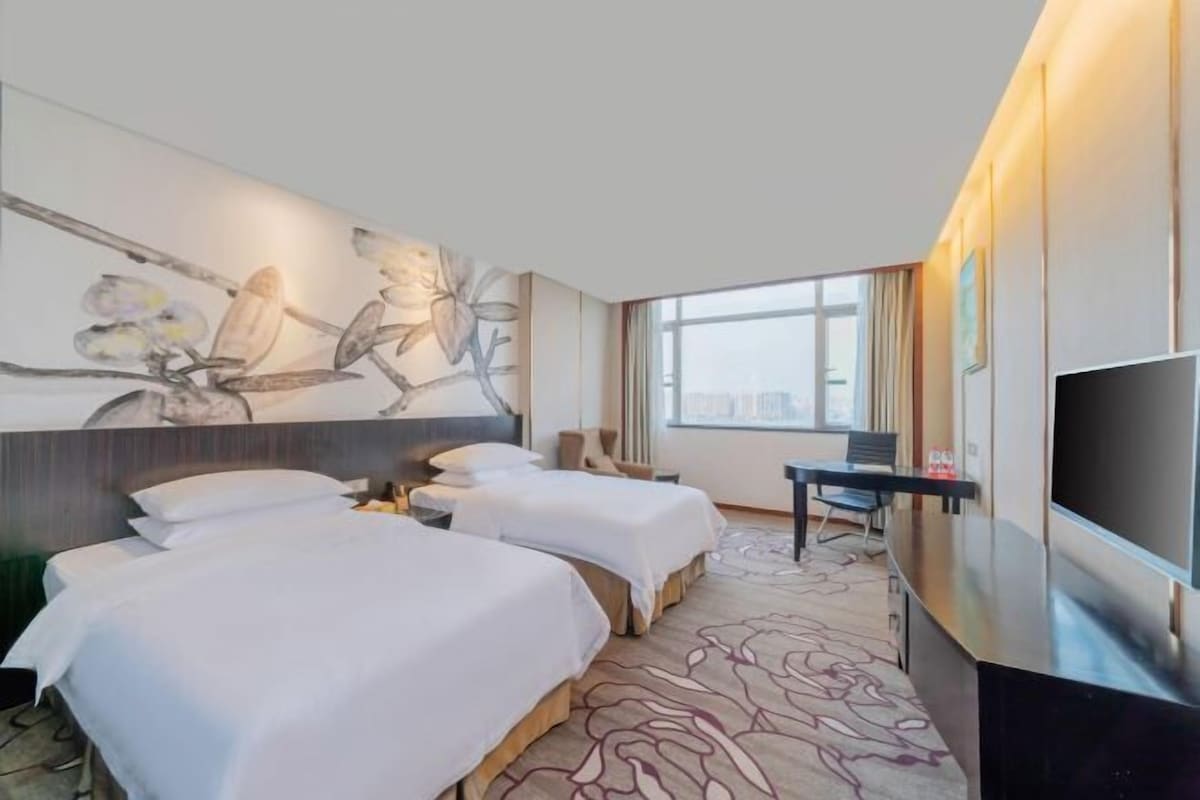 A hotel room with two beds, a large TV, a desk, and a city view.